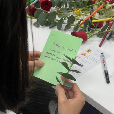 Person holding a green card with text next to flowers and stationery on a table