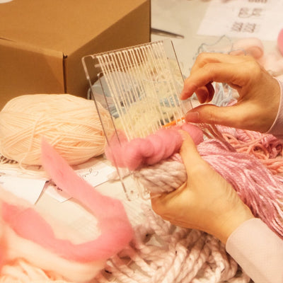 People working with pink yarn at a table, with a box and other materials in the background.