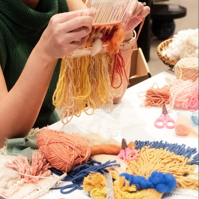Woman in a green shirt holding yarn and smiling, with a table of craft materials in front of her.